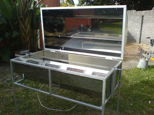 Stainless steel commercial hog roast machine with the lid open, in a garden