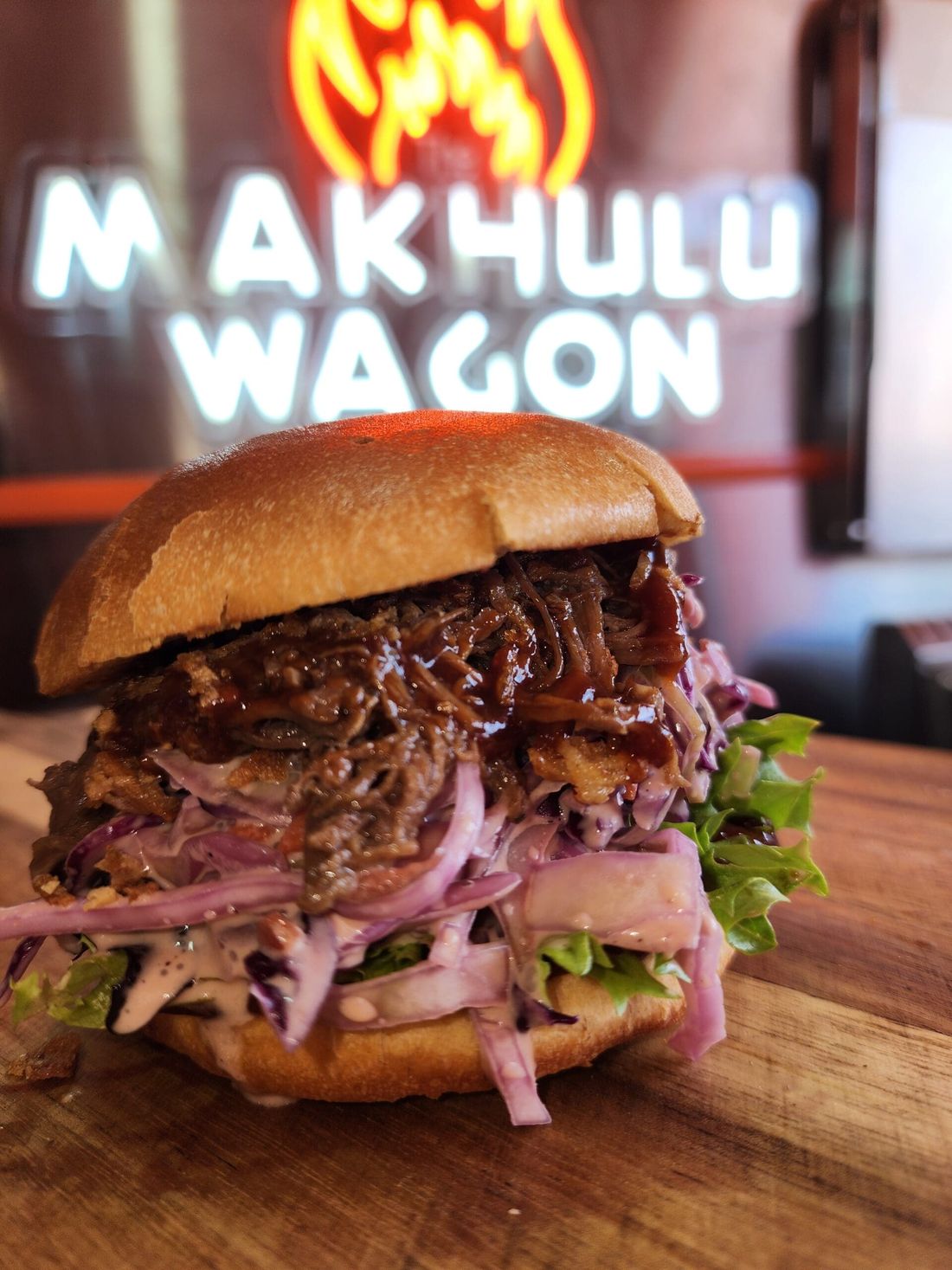 Pulled pork brioche burger in front of the Makhulu Wagon neon sign